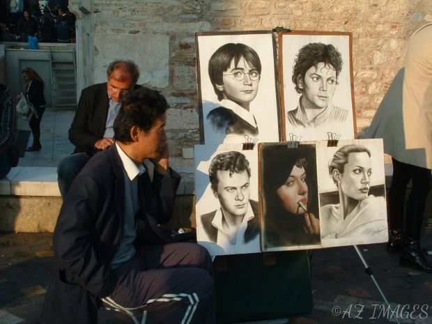 An Artists sits next to  his drawings of famous people.